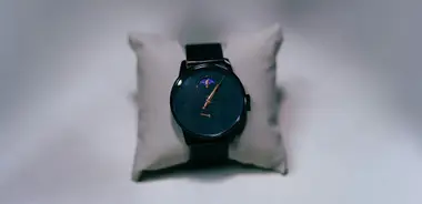 Black wristwatch with a moon phase dial on a small grey pillow